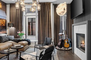 A modern living room with a fireplace, a sofa, a coffee table, and a guitar. - Songwriters' Retreat: 4BR, Rooftop Sauna & Bar (Nashville)
