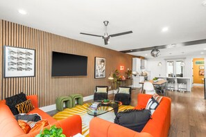 A modern living room with orange sofas, a glass coffee table, and a flat-screen TV mounted on the wall. - 10 Beds | Minutes to Broadway, Gulch & 12 South (Nashville)