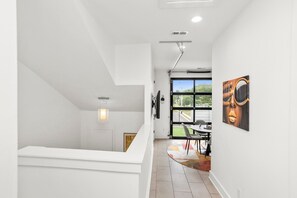 Ein modernes Interieur mit einer weißen Wendeltreppe, die zu einem Balkon führt, einem Essbereich mit Aussicht und einem großen Fenster.