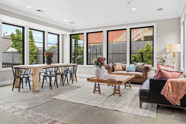 A spacious living room with a dining area, large windows, and a view of the outside.