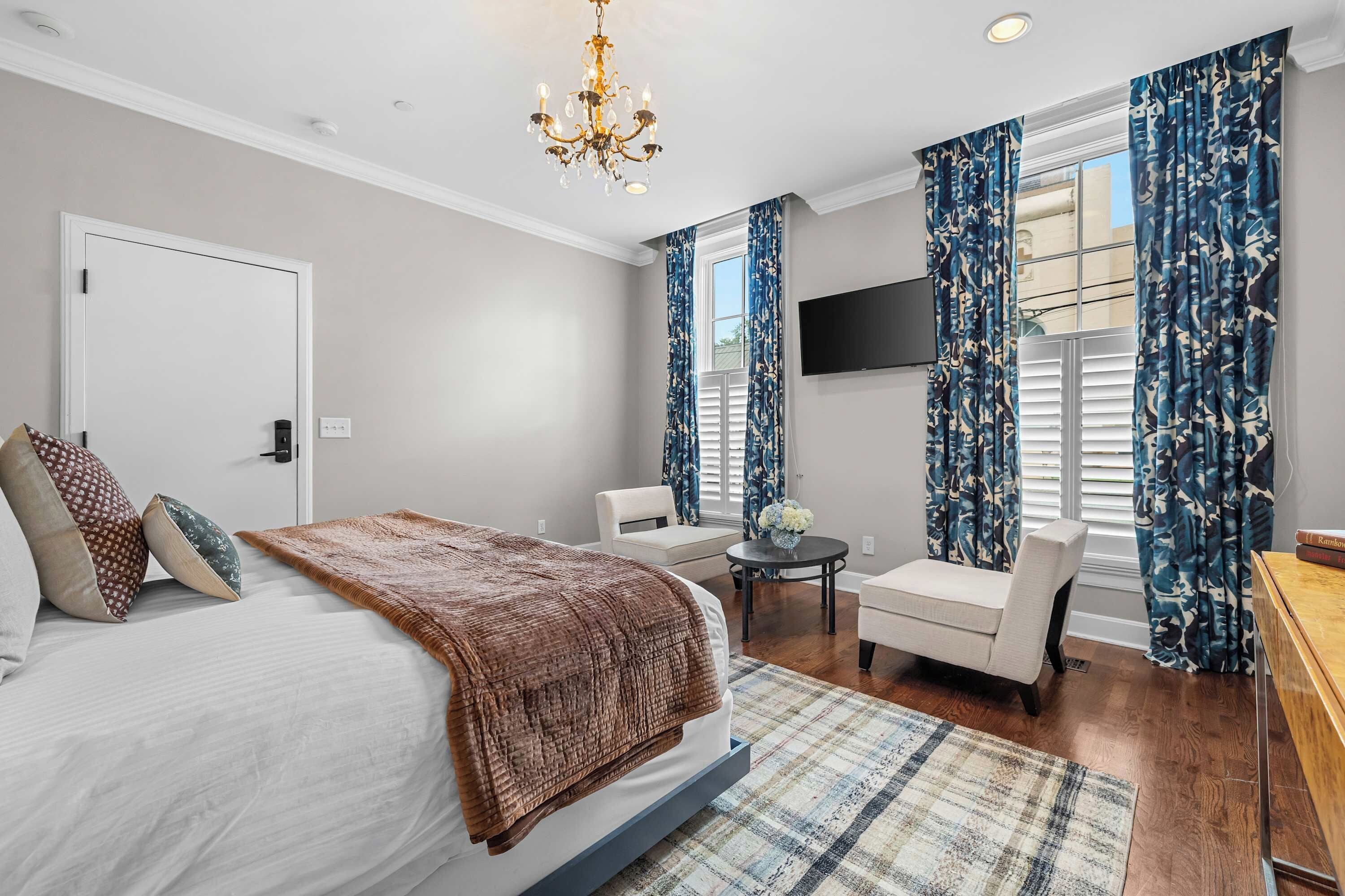 A bedroom with a bed, a chair, a TV, and a window with curtains.