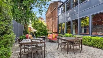Eine Terrasse im Freien mit Holztischen und -stühlen, einem roten Sofa und einer Feuerstelle.