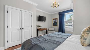 Een slaapkamer met een bed, bureau, stoel, televisie en een raam met gordijnen.