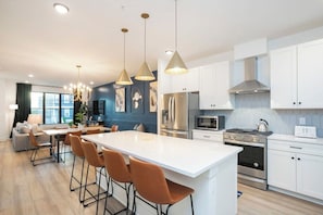 A modern kitchen with white cabinets, stainless steel appliances, and a central island with bar stools. - 2 Mi to DT + King Beds & Garage (Nashville)