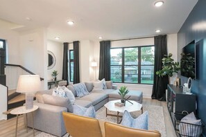 A modern living room with a sectional sofa, a coffee table, and a TV on a wall. - 2 Mi to DT + King Beds & Garage (Nashville)
