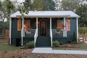 A two-story house with a porch, a front door, and a small garden area. - Leipers Fork Bungalow | Hot Tub & Firepit (Franklin)