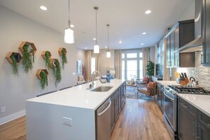 A modern kitchen with a central island, stainless steel appliances, and wooden hexagonal shelves with greenery. - Rooftop, Grill, Garage, Near Broadway (Nashville)