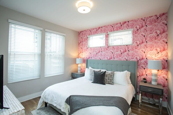 A bedroom with a large bed, two bedside tables with lamps, and a wall with a pink flamingo pattern. - Rooftop, Grill, Garage, Near Broadway (Nashville)