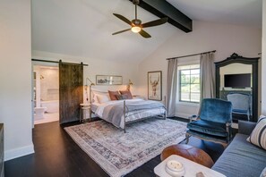 A bedroom with a bed, a ceiling fan, a large window with curtains, a chair, and a sofa. - Luxury Franklin Farmhouse (Franklin)