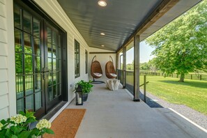 A covered porch with large windows, two hanging chairs, and a view of a grassy landscape. - Luxury Franklin Farmhouse (Franklin)