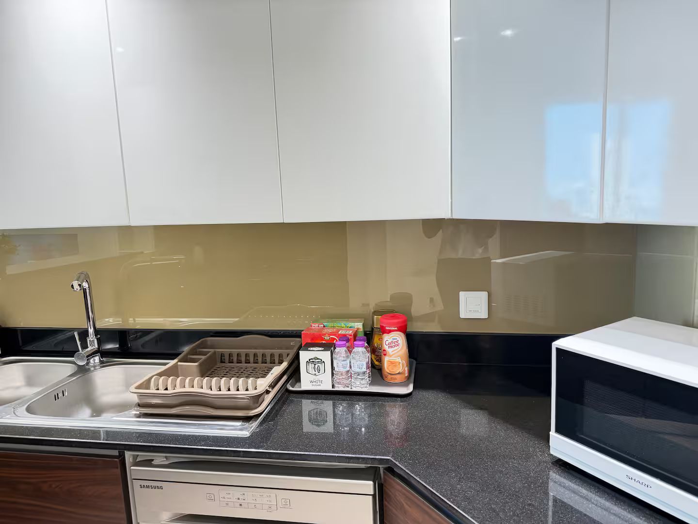 A kitchen with a dishwasher, a microwave, and a countertop with various items including a coffee maker, a water bottle, and a box of sugar.