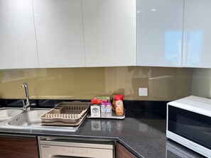 Una cocina con lavavajillas, microondas y una encimera con varios objetos, incluyendo una cafetera, una botella de agua y un paquete de azúcar.