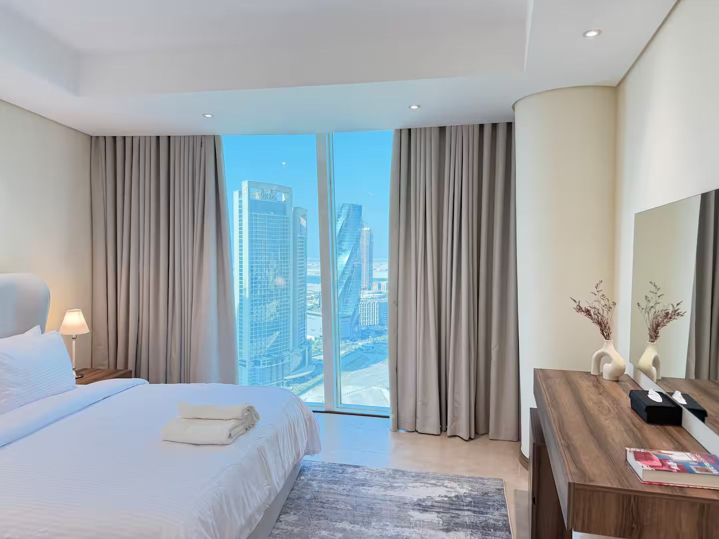 Une chambre d’hôtel avec un lit, un bureau, un miroir et une vue sur les bâtiments de la ville.