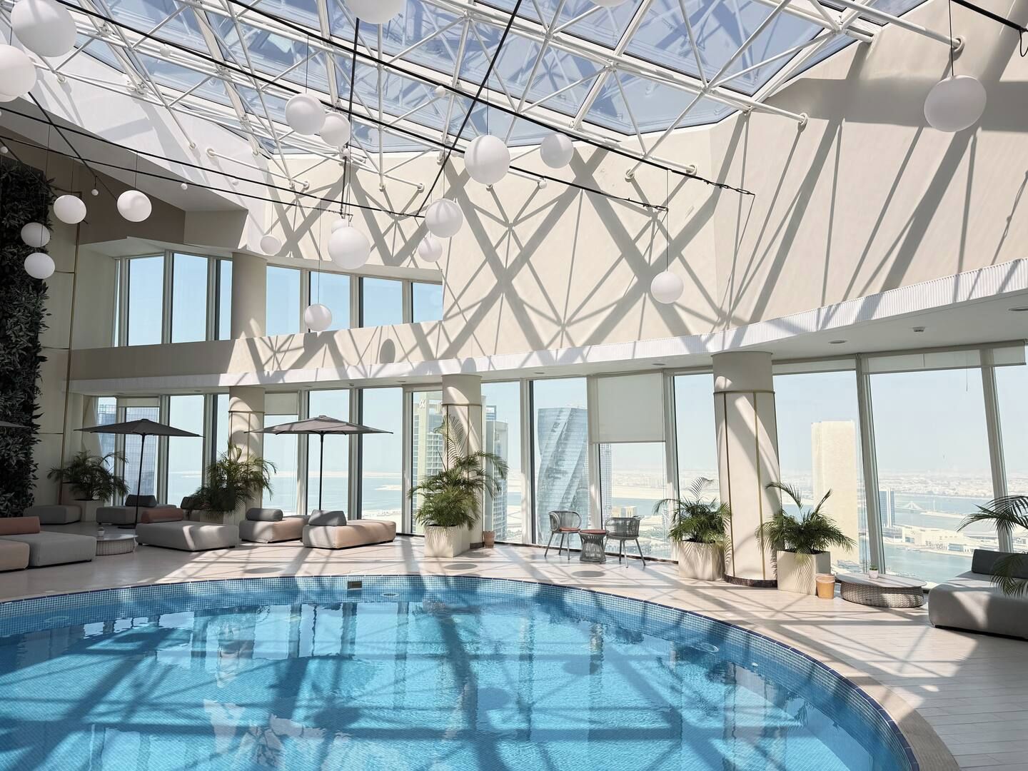 Un espace piscine intérieur moderne doté d’un plafond en verre, de sièges et de plantes en pot.