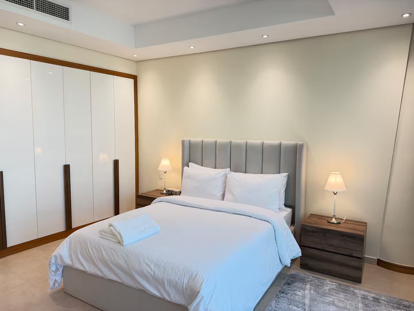 A modern bedroom with a large bed, two bedside tables with lamps, a wardrobe, and a ceiling light.