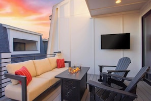A balcony with a sofa, chairs, a table with a fire feature, and a TV mounted on the wall. - Printer's Alley Vibes Rooftop Fire Table + Karaoke (Nashville)
