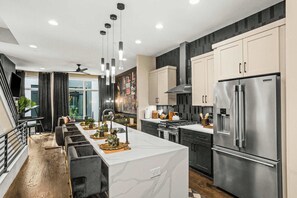 A modern kitchen with a large island, stainless steel appliances, and a dining area with a view. - Printer's Alley Vibes Rooftop Fire Table + Karaoke (Nashville)