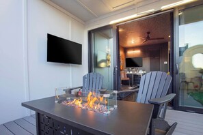 A modern outdoor dining area with a fire feature, two Adirondack chairs, and a flat-screen TV mounted on the wall. - Printer's Alley Vibes Rooftop Fire Table + Karaoke (Nashville)
