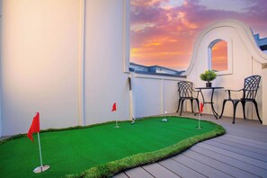 Um campo de mini golfe com vista para o pôr do sol, uma pequena mesa com cadeiras e um arco decorativo.