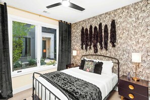 Une chambre à coucher comprenant un lit, une table de chevet, une lampe, une fenêtre avec des rideaux et un papier peint à motifs.
