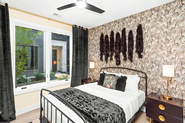 Quarto com cama, mesa de cabeceira, luminária, janela com cortinas e papel de parede estampado.