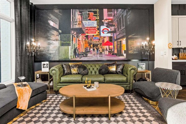Un salon moderne avec un canapé vert, une table basse ronde et un grand téléviseur diffusant une scène de rue urbaine.
