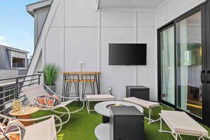A rooftop terrace with outdoor seating, a flat-screen TV, and a fire pit. - Disco Dream | 4BR Rooftop Sauna & Wellness Studio (Nashville)
