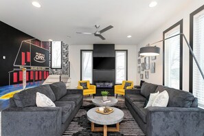 Een moderne woonkamer met een hoekbank, twee gele fauteuils, een ronde salontafel en een flatscreen televisie.