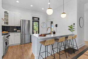 A modern kitchen with white cabinetry, stainless steel appliances, a central island with bar stools, and pendant lighting. - Historic East Nash | 5 Kings, 5 Baths, Walkable (Nashville)