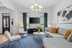 A modern living room with a sofa, armchairs, a coffee table, and a flat-screen TV mounted on the wall. - Historic East Nash | 5 Kings, 5 Baths, Walkable (Nashville)