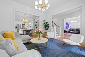 A spacious living room with a grey sofa, a round coffee table, and a white armchair. There is a vase with flowers on the coffee table. - Historic East Nash | 5 Kings, 5 Baths, Walkable (Nashville)