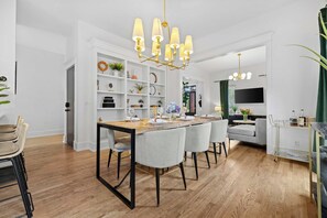 A modern dining area with a wooden table, grey chairs, and a chandelier. - Historic East Nash | 5 Kings, 5 Baths, Walkable (Nashville)