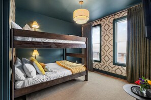 A bunk bed room with a patterned wall, a window with curtains, and a table with a vase of flowers. - Minutes to Downtown | Rooftop Skyline Views (Nashville)