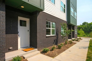 A modern building with a brick facade, numbered 1415, featuring a white door and windows, and a small garden area with plants and a pathway. - Near Downtown | Rooftop | Games (Nashville)