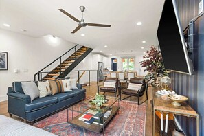 A spacious living room with a blue sofa, leather chairs, a coffee table, and a staircase leading to an upper level. - 12 South | 7 Beds | 2mi to Broadway (Nashville)