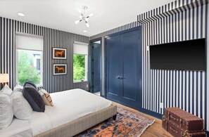 A bedroom with a bed, a TV, a wardrobe, and a window with a view of greenery. - 12 South | 7 Beds | 2mi to Broadway (Nashville)