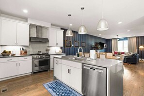 Een moderne keuken met witte kastjes, roestvrijstalen apparatuur en hangende lampen.