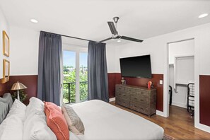 Een slaapkamer met een groot bed, een plafondventilator, een televisie, een dressoir en een balkon met gordijnen.