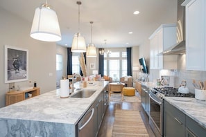 A modern kitchen with a marble countertop, stainless steel appliances, pendant lighting, and a dining area with a sofa and ottoman. - Rooftop City Views, Garage, Near Broadway (Nashville)