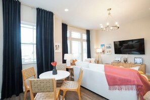 A hotel room with a bed, a TV, a dining table with chairs, and a window with curtains. - Rooftop City Views, Garage, Near Broadway (Nashville)