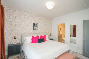 A bedroom with a patterned wallpaper, a bed with white bedding and colorful pillows, a bedside table with a lamp, and a mirror on the wall. - Rooftop City Views, Garage, Near Broadway (Nashville)