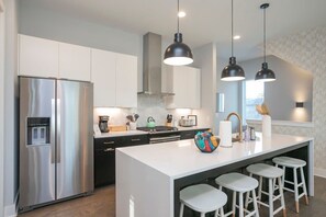 A modern kitchen with a stainless steel refrigerator, a central island with stools, pendant lighting, and a view of the outdoors. - 1 Mile to Downtown 4BR w/Rooftop (Nashville)