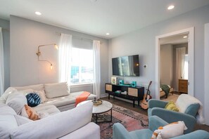A modern living room with a sofa, armchairs, a coffee table, a TV, and a guitar. - 1 Mile to Downtown 4BR w/Rooftop (Nashville)