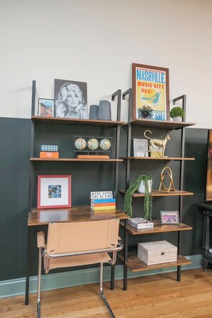 Een kamer met een zwart-wit gestreepte muur, een houten bureau met een leren fauteuil, en planken met diverse decoratieve objecten, waaronder een ingelijst schilderij, wereldbollen en een boek met de titel 'WORK HARD AND BE KIND'.