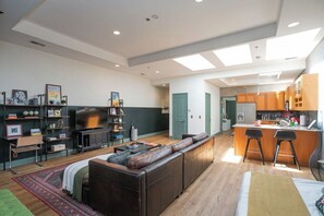 A modern living room with a sofa, a TV, and a kitchen area with a bar. - Penthouse Above Music & Bars (Nashville)