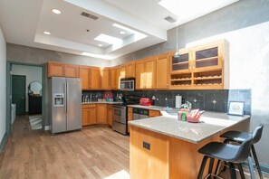 A modern kitchen with wooden cabinets, stainless steel appliances, and a central island with bar stools. - Penthouse Above Music & Bars (Nashville)