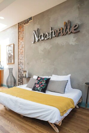A bed with a white and yellow bedspread, two pillows, and a wall with a 'Nashville' sign. - Penthouse Above Music & Bars (Nashville)