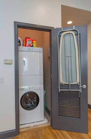 A laundry area with a washing machine and dryer, a ironing board, and laundry supplies. - Penthouse Above Music & Bars (Nashville)