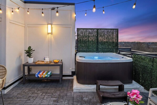 Terraço no telhado com hidromassagem, luzes de Natal, mesa com toalhas e vista para a cidade.