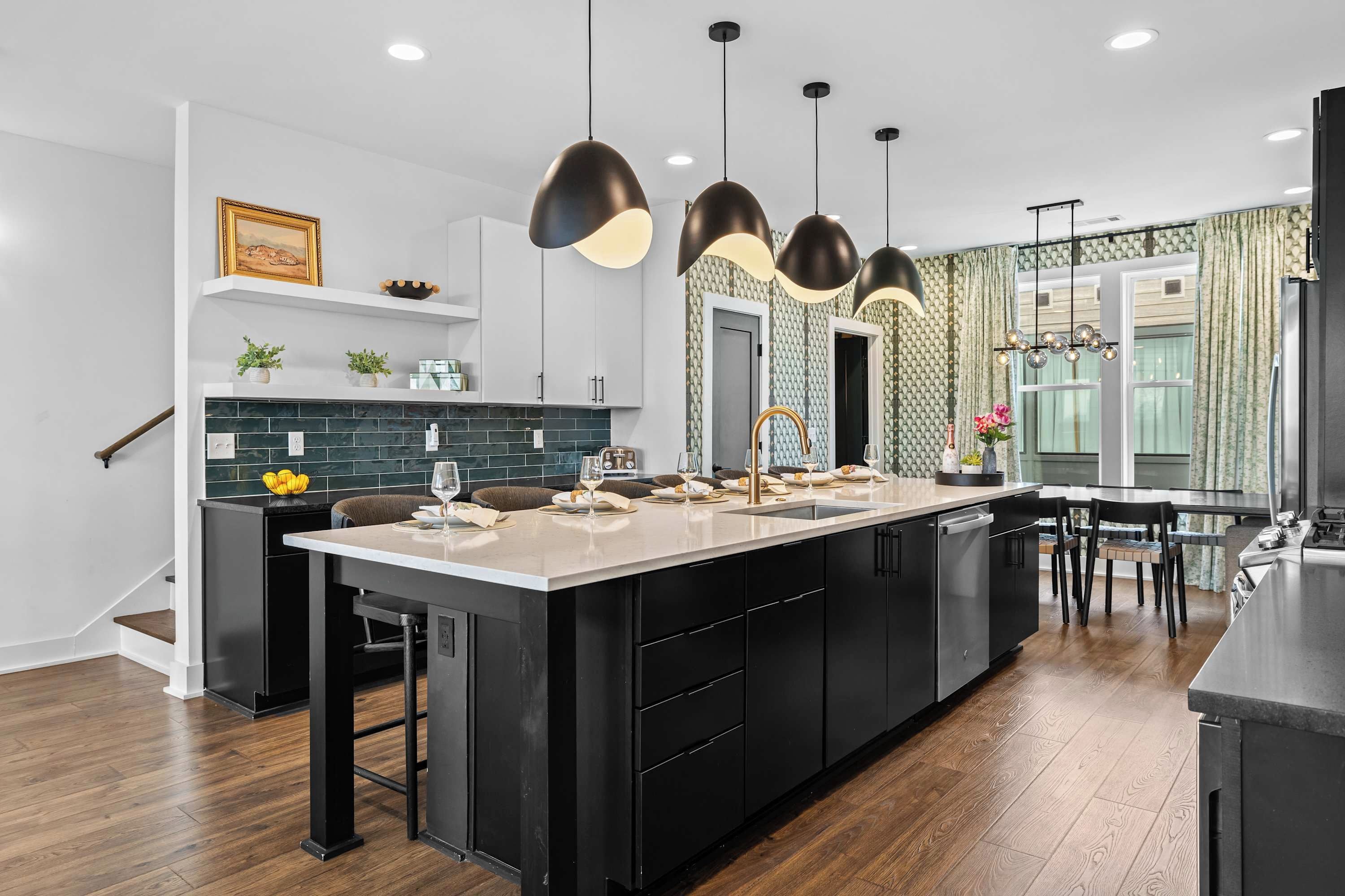 A modern kitchen with a large island, black cabinetry, and pendant lighting.